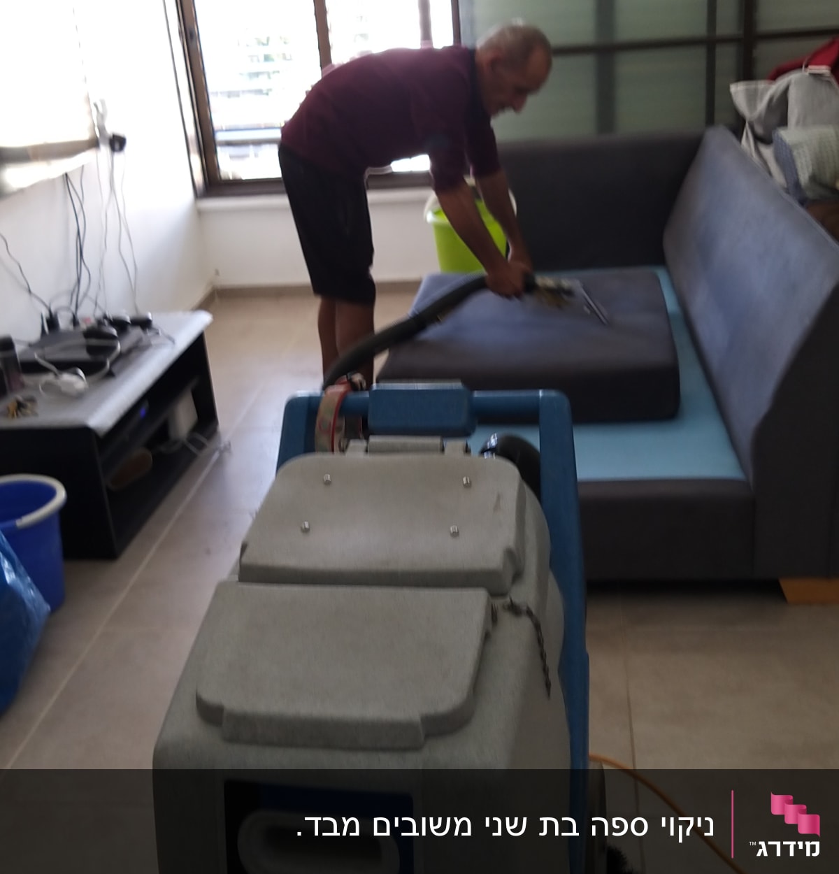 אדם מנקה ספה עם מכונת ניקוי מקצועית